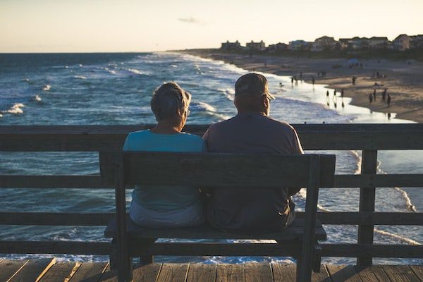 A senior couple is able to afford vacation thanks to their retirement investments. They accumulated enough wealth to sit and watch the ocean waves roll into the beach.